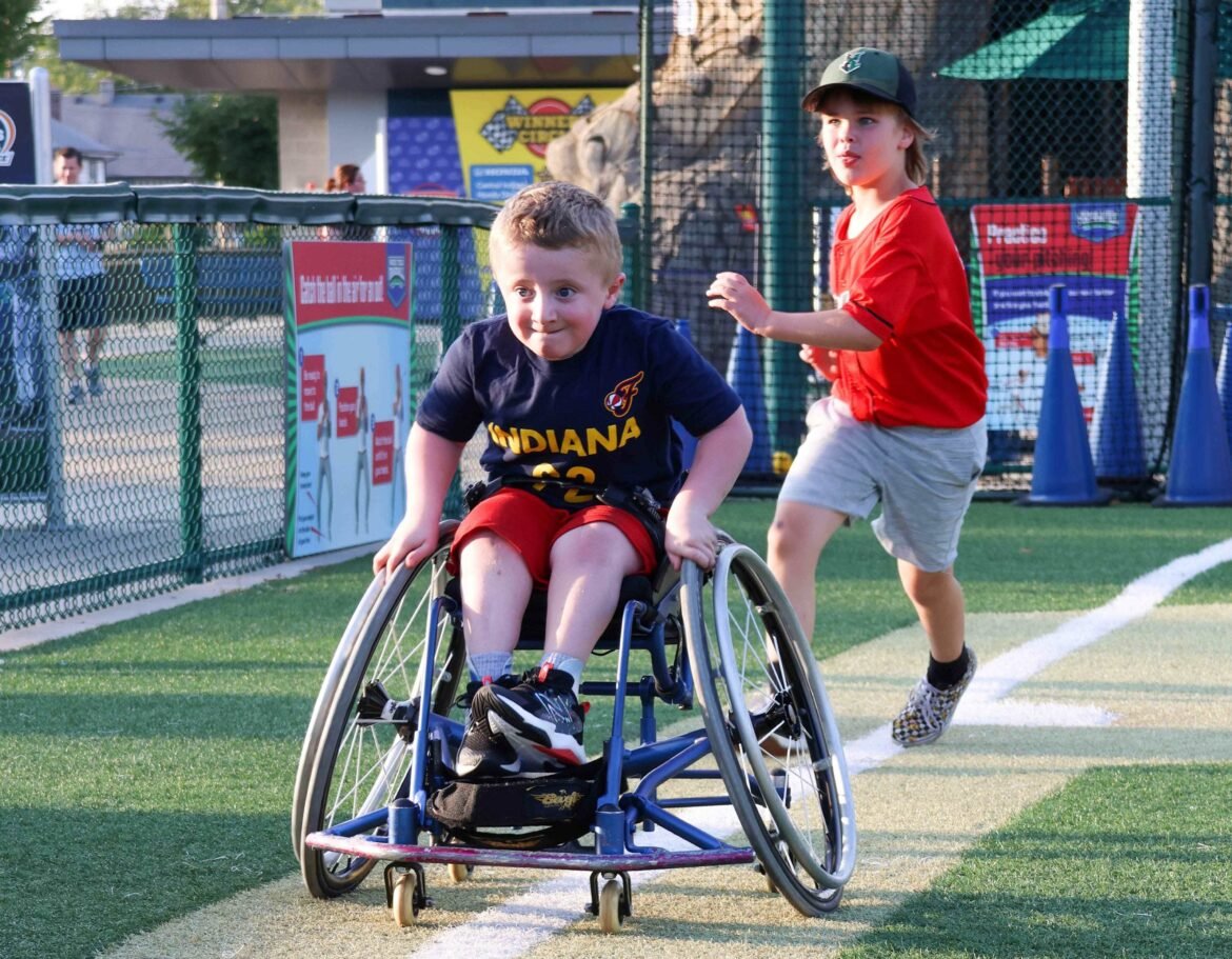 Kid in a wheelchair going around the bases on a baseball diamond.